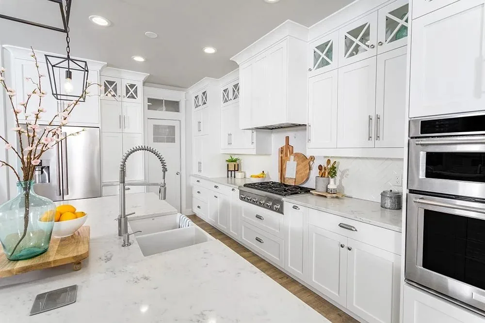 A white painted kitchen with full-height cabinets, glass-front uppers and a marble island